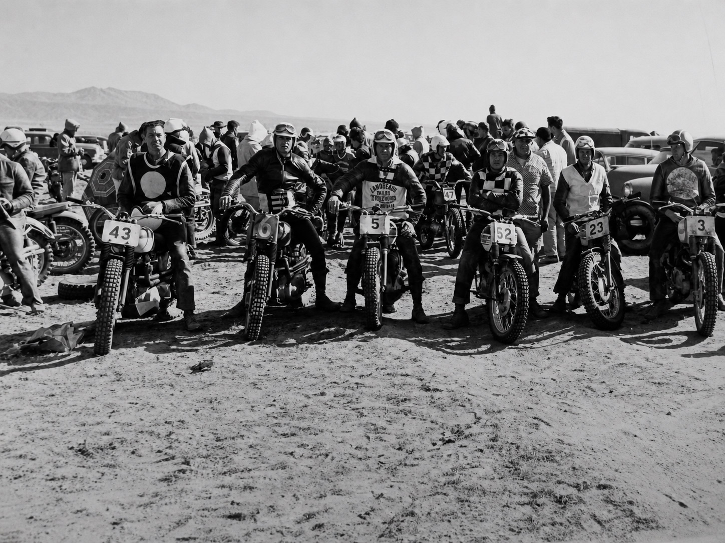 Vintage motorcycle riders lined up together in the desert.